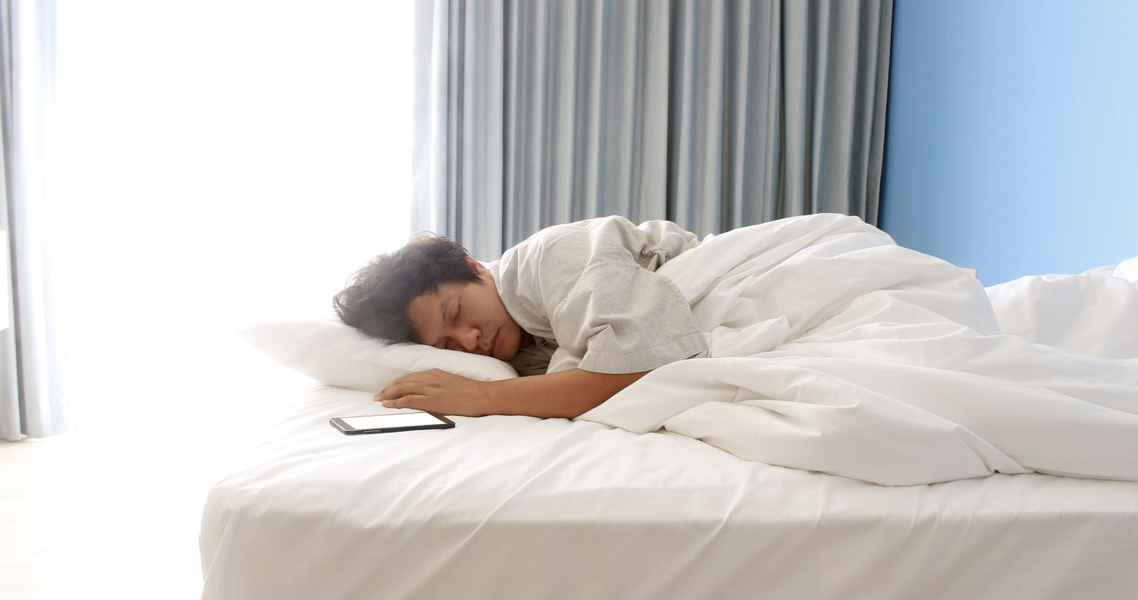Person, die auf einem Bett mit weißen Laken schläft.